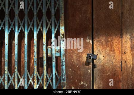 Altes goldenes Stahlschloss und beschädigte und verrostete Stahltür an Holztür. Verriegelt an Holztür mit altem Metallladen und Falttor. Alter Arbeitsauftrag Stockfoto