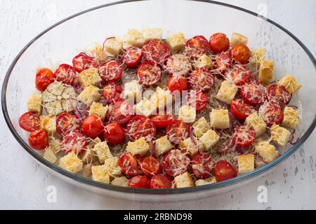 Gebackene Kirschtomaten, Croutons, rote Zwiebeln, Knoblauch, Gewürze und Käse in einem Backblech aus Glas auf hellgrauem Hintergrund, Draufsicht. Italienisch kochen Stockfoto