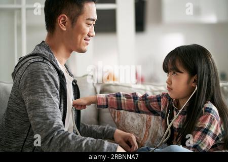 Junger asiatischer Vater, der Arzt- und Patientenspiel mit siebenjähriger Tochter zu Hause spielt Stockfoto