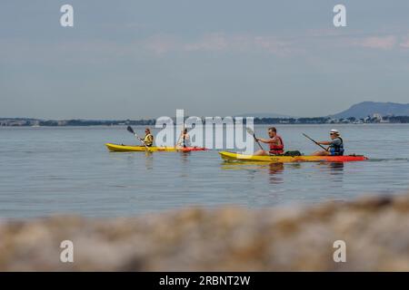 Eine Gruppe von Kanufahrern, die entlang der Küste von Alcanada, Alcudia, segeln. Mallorca, Balearen, Spanien. Stockfoto