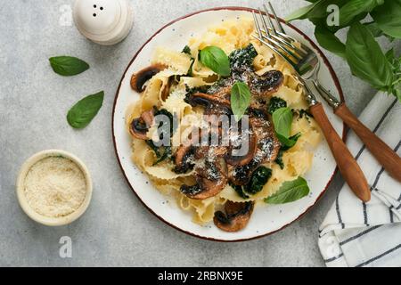 Cremige Alfredo-Pasta. Italienische Pasta Fettuccini mit Pilzen, Hühnerfleisch, Spinat, Basilikum und Sahne auf grauem Stein- oder Betonhintergrund. Trad Stockfoto