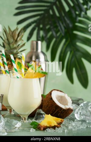 Pina Colada. Traditioneller karibischer Cocktail aus Rum, Ananassaft und Kokosnusscreme mit tropischen Früchten und Barutensilien auf frischem grünen Hintergrund. Stockfoto