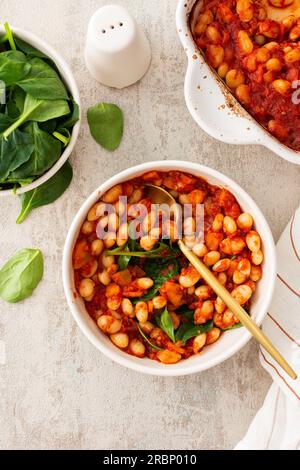 Gesundes Frühstück und Mittagessen, gedünstete weiße Bohnen mit Karotten, Zwiebeln und Tomaten mit Spinatblättern, eine Schüssel Bohnen und Spinat Stockfoto