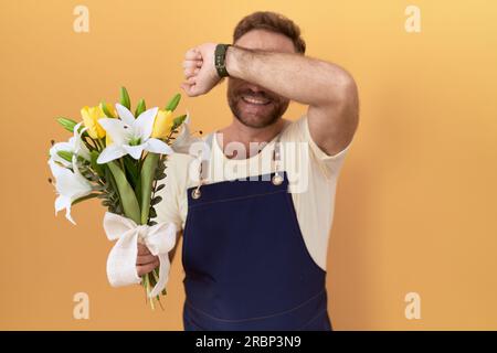 Ein Mann mittleren Alters mit einem Bart-Blumenladen, der Blumen hält und fröhlich lächelt. Er spielt ein Auge auf das Baby, wobei die Hände das Gesicht zeigen. Überrascht und verlassen Stockfoto