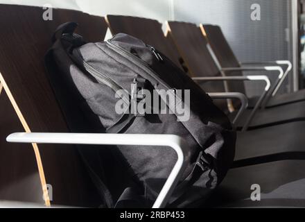 Ein schwarzer Rucksack, der in einer Reihe leerer Sitze in einem Wartebereich sitzt Stockfoto