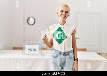 Junge blonde Frau, die pakistanische Flagge hält und am Wahlcollege lächelt Stockfoto