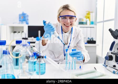 Junge blonde Wissenschaftlerin, die im Labor Flüssigkeit auf das Reagenzglas gießt Stockfoto