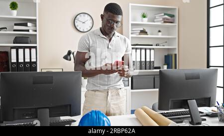 afroamerikanischer Männerarchitekt, der im Büro mit einem Smartphone arbeitet Stockfoto