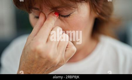 Frau mittleren Alters, die Kopfschmerzen hat, wenn sie auf dem Sofa zu Hause sitzt Stockfoto