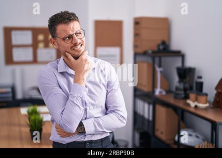 Junger spanischer Mann im Büro, der sich Sorgen um eine Frage machte, besorgt und nervös mit der Hand am Kinn Stockfoto
