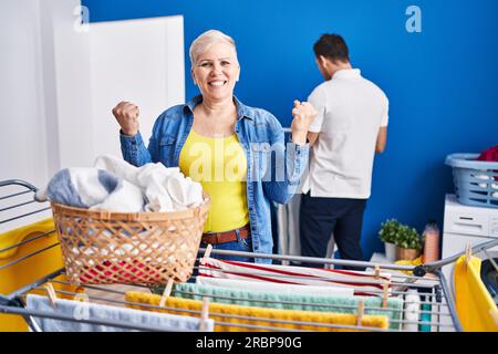 Hispanische Mutter und Sohn hängen Kleider an der Wäscheleine und schreien stolz, feiern den Sieg und Erfolg sehr aufgeregt mit erhobenen Armen Stockfoto
