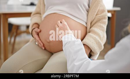 Junge schwangere Gynäkologin und Patientin bei der Bauchuntersuchung mit Stethoskop in der Klinik Stockfoto