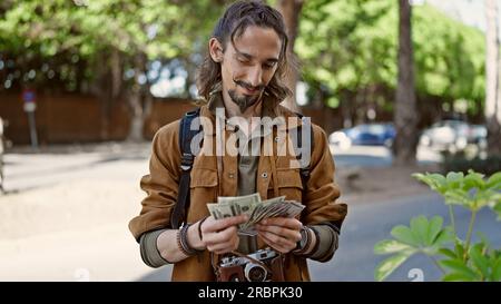 Junger hispanischer Tourist mit Rucksack, der im Park Dollars zählt Stockfoto