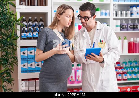 Mann und Frau, Apotheker und schwangere Klientin, die Smartphone und Touchpad benutzen und in der Apotheke sprechen Stockfoto