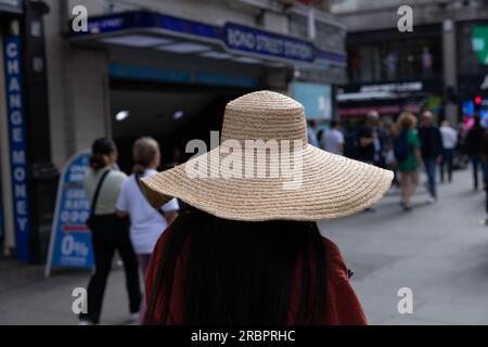 Frau mit Strohhut, die lange Oxford Street entlang der U-Bahnstation Bond Street im Zentrum von London, England, Großbritannien, spaziert Stockfoto