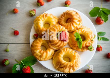 Gekochte süße Cupcakes mit frischen Erdbeeren und Minze auf einem Holztisch. Stockfoto