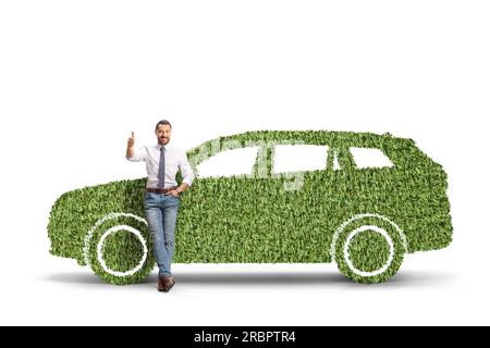 Das Porträt eines Mannes, der sich auf ein grünes Auto aus Gras lehnt und die Daumen nach oben bewegt, isoliert auf weißem Hintergrund Stockfoto
