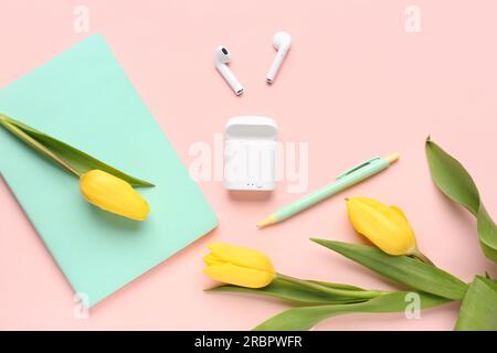 Moderne Kopfhörer, Notizbuch, Stift und wunderschöne Tulpenblumen auf pinkfarbenem Hintergrund Stockfoto