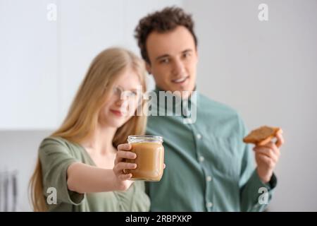 Junge Frau mit Nussbutter in der Hand und hübscher Mann mit Toast in der Küche Stockfoto