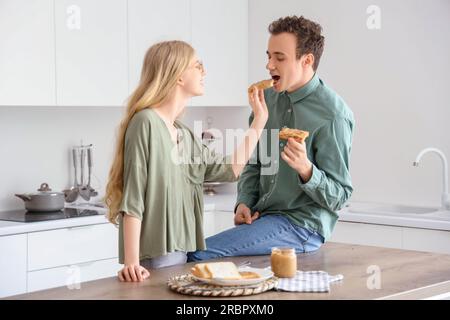 Junge Frau füttert ihren Freund mit leckerem Toast mit Nussbutter in der Küche Stockfoto