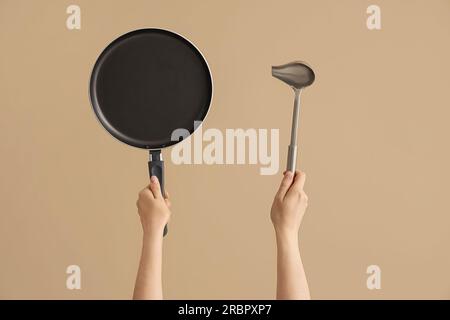 Weibliche Hände mit Bratpfanne und Kelle auf braunem Hintergrund Stockfoto