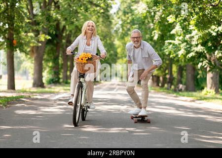 Moderne Rentner. Glückliches Seniorenpaar Mit Fahrrad Und Skateboard Im Park Stockfoto