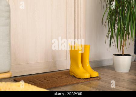 Gelbe Gummistiefel auf der Matte in der Nähe der Tür Stockfoto