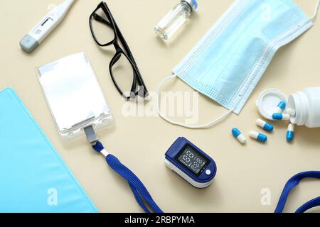 Badge, Pulsoxymeter, Schutzbrille, Maske und Pillen auf beigefarbenem Hintergrund Stockfoto