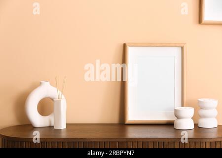 Eine Flasche Reed-Diffusor und ein leerer Rahmen auf dem Tisch nahe der beigen Wand im Raum Stockfoto