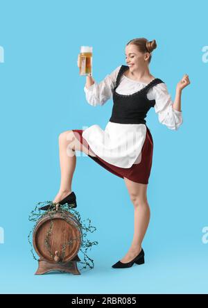 Wunderschöne Oktoberfest-Kellnerin mit Bier und Fass auf blauem Hintergrund Stockfoto