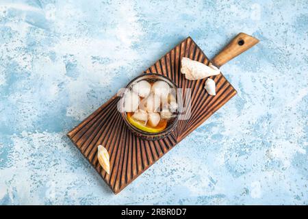 Gehen Sie an Bord mit einem Glas kalten Cuba Libre Cocktail und Muscheln auf blauem Hintergrund Stockfoto