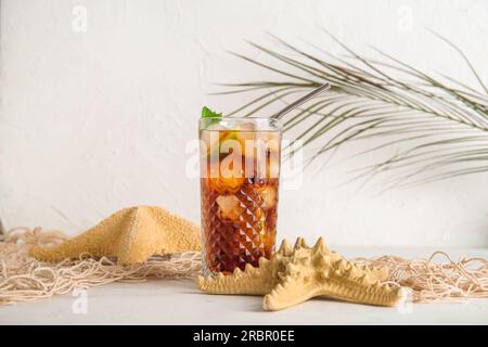 Ein Glas kalter Cuba Libre Cocktail, Seesterne und Palmenblätter auf weißem Hintergrund Stockfoto
