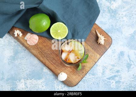 Gehen Sie an Bord mit einem Glas kalten Cuba Libre Cocktail und Muscheln auf blauem Hintergrund Stockfoto