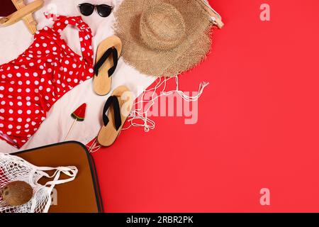 Koffer mit verschiedenen Strandaccessoires auf rotem Hintergrund. Reisekonzept Stockfoto