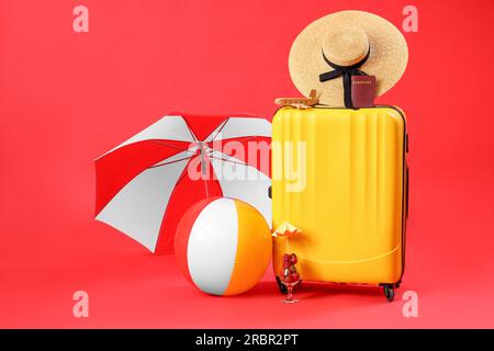 Koffer mit Reisepass und verschiedenen Strandaccessoires auf rotem Hintergrund. Reisekonzept Stockfoto