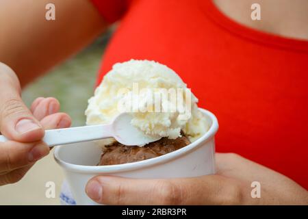 Nahaufnahme weiblicher Hände im Freien, mit einer Portion Eiscreme aus einem kleinen Pappbecher, mit Kopierraum. Stockfoto