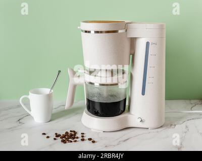 Die automatische Filterkaffeemaschine bereitet morgens ein Getränk zu. Elektrische Kaffeemaschine füllt Glaskanne mit heißem schwarzem Kaffee auf einer Marmorablage zu Hause. Stockfoto
