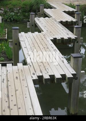 Harmonie im Ritsurin Garden, Japan: Eine hölzerne Brücke über den Teich ist in einem Zickzack-Design gehalten, da das Böse nicht in geraden Linien auf die andere Seite überqueren kann. Stockfoto