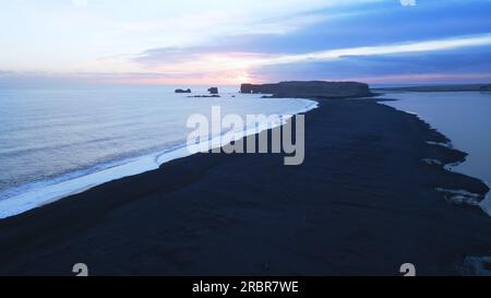 Luftaufnahme des schwarzen Sandstrands mit Bergen und großen Steinen in island, wunderschöne natürliche Landschaft am Reynisfjara Strand. Isländische Landschaft mit atlantik an der Küste. Zeitlupe. Stockfoto