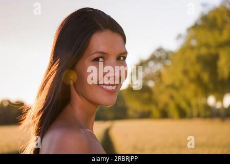 Schöne junge Frau, die im Weizenfeld steht und lächelt Stockfoto