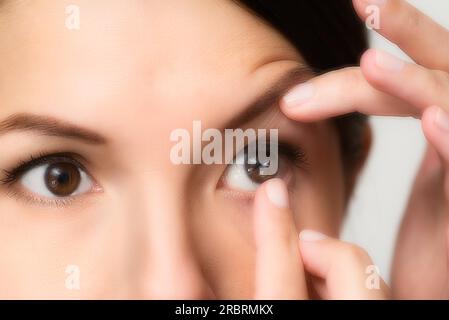 Eine Frau, die gerade eine Einweg-Kontaktlinse aus Plastik in ihr Auge steckt, um ihr Sehvermögen zu korrigieren, hat sie am Ende ihres Fingers vor ihrem Gesicht ausgeglichen Stockfoto