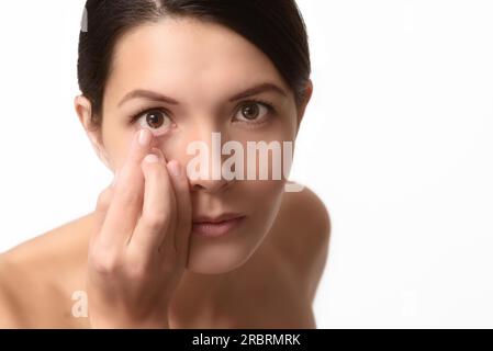 Eine Frau, die gerade eine Einweg-Kontaktlinse aus Plastik in ihr Auge steckt, um ihr Sehvermögen zu korrigieren, hat sie am Ende ihres Fingers vor ihrem Gesicht ausgeglichen Stockfoto