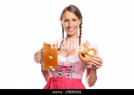 Lächelnde junge Frau mit geflochtenem Haar in einem traditionellen, roten deutschen oder bayerischen Dirndl, die einen Glastank mit Bier und Brezel in der Hand hält Stockfoto