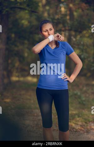 Sportlerin, Schweiß von der Stirn auf ihrem Armband abwischen, da sie während ihrer Übungen auf einem Waldweg macht eine Pause Stockfoto