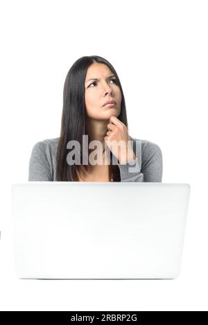 Attraktive, stilvolle junge Geschäftsfrau mit besorgtem Stirnrunzeln, die hinter ihrem Laptop an ihrem Schreibtisch sitzt und mit der Hand in die Luft starrt Stockfoto