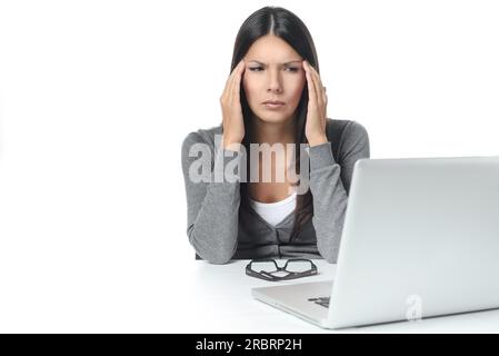 Junge Frau leidet unter Kopfschmerzen oder Migräne mit Blick auf Laptop auf dem Tisch. isoliert auf weißem Hintergrund Stockfoto