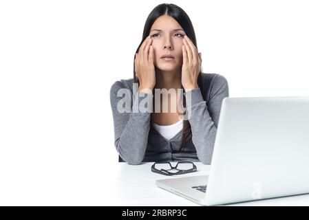 Junge Frau leidet unter Kopfschmerzen oder Migräne mit Blick auf Laptop auf dem Tisch. isoliert auf weißem Hintergrund Stockfoto