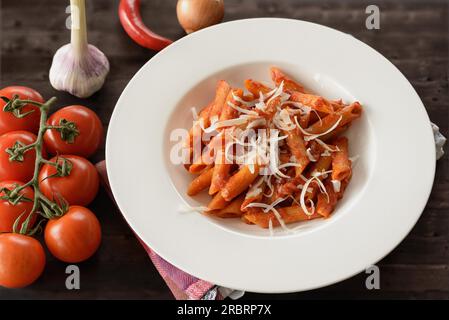 Teller Penne Pasta mit Sauce arrabiata, einer pikanten Sauce mit Knoblauch, Tomaten, Chili und Olivenöl, garniert mit frischem Basilikum und Parmesan Stockfoto