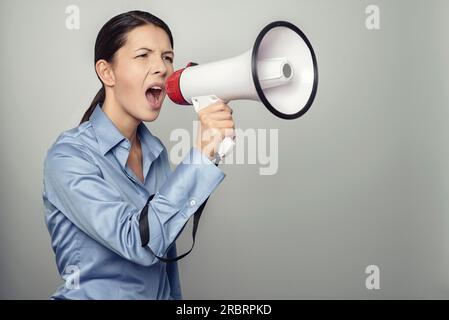Eine Frau spricht über ein Megaphon, während sie eine öffentliche Rede hält, an einem Protest teilnimmt oder eine Rallye oder Beförderung organisiert, über Grau mit Werbetexten Stockfoto