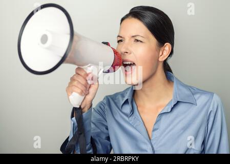 Eine Frau spricht über ein Megaphon, während sie eine öffentliche Rede hält, an einem Protest teilnimmt oder eine Rallye oder Beförderung organisiert, über Grau mit Werbetexten Stockfoto